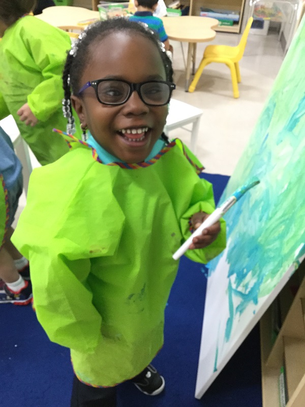 Naijah uses green & blue paint to create an art piece on a canvas